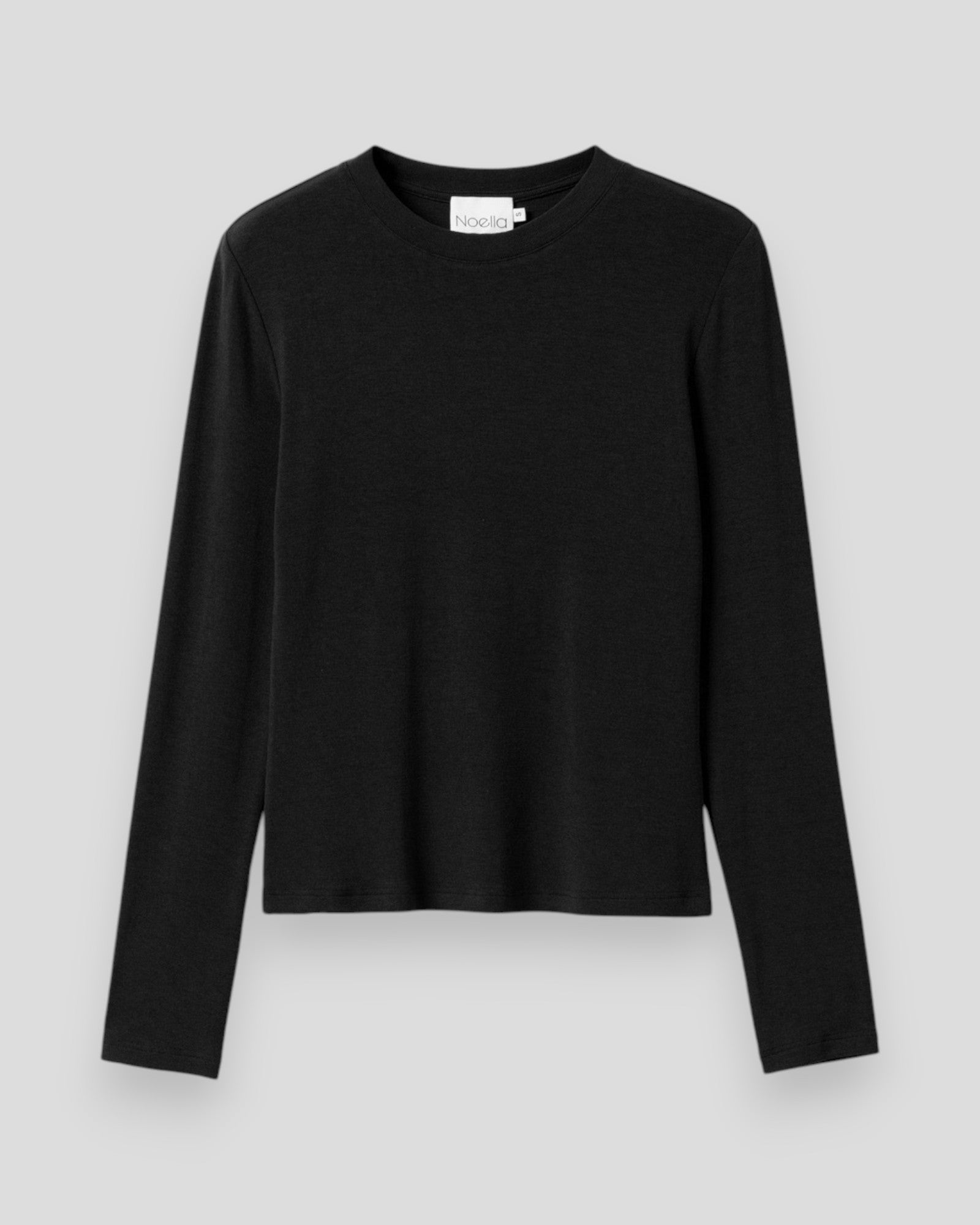 Sort Noella Lidie LS Top, langærmet top i blødt stof med rund hals, vist i et billede med chokoladefarvet baggrund.