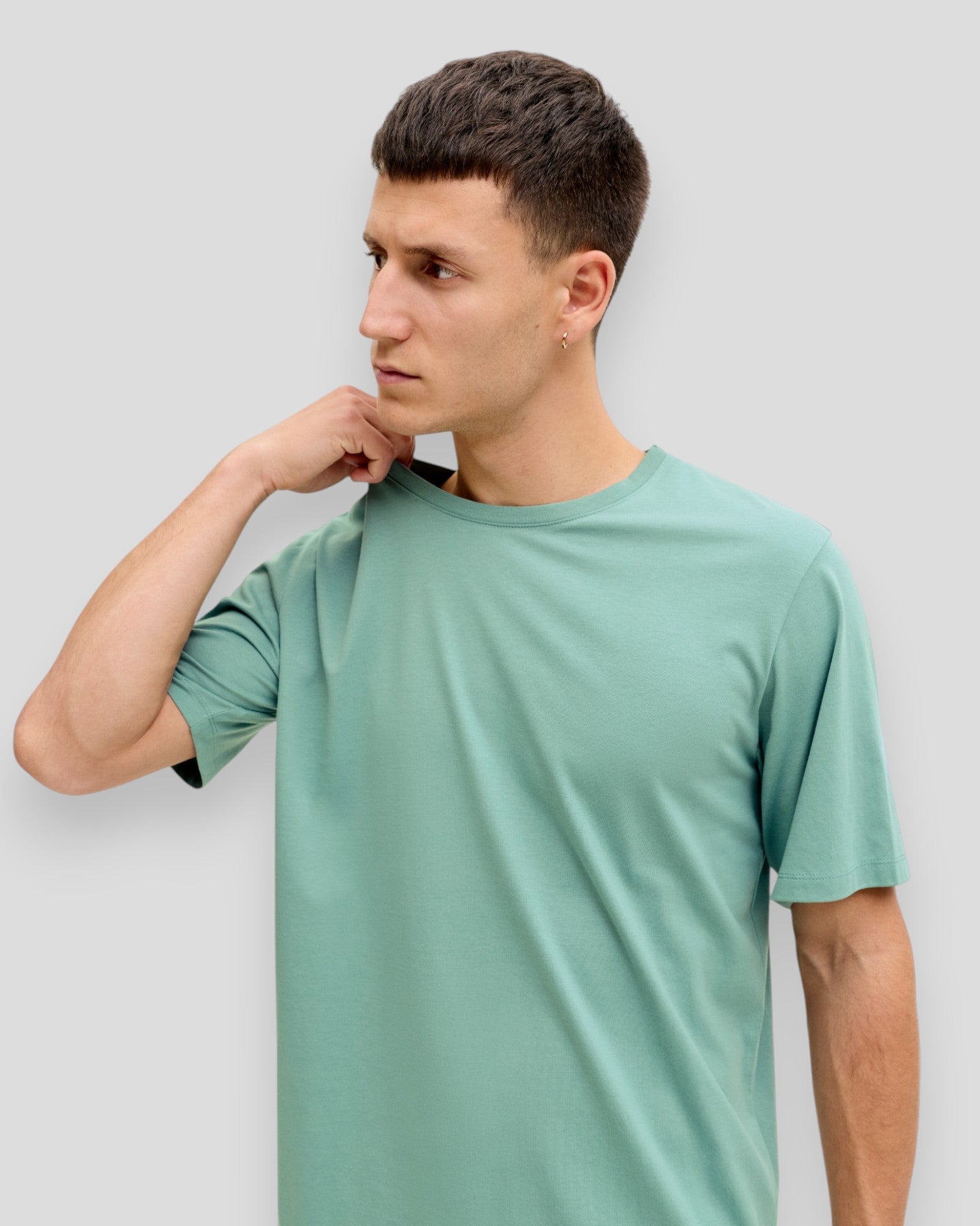 Menneskehånd holder en mineralblå jack & jones økologisk basic T-shirt med O-udskæring, vises på flat.