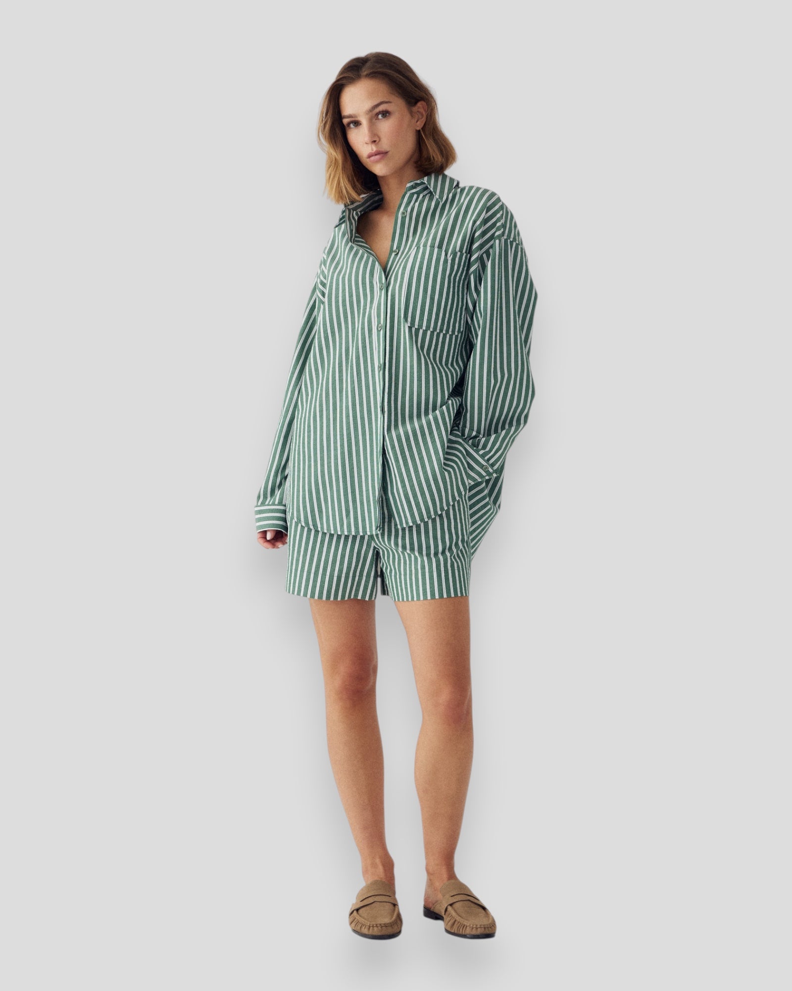 Kvinde i Noella N-Marlon skjorte i grønstribet stof med lange ærmer og krave, afslappet stil, foran et lyst baggrund.