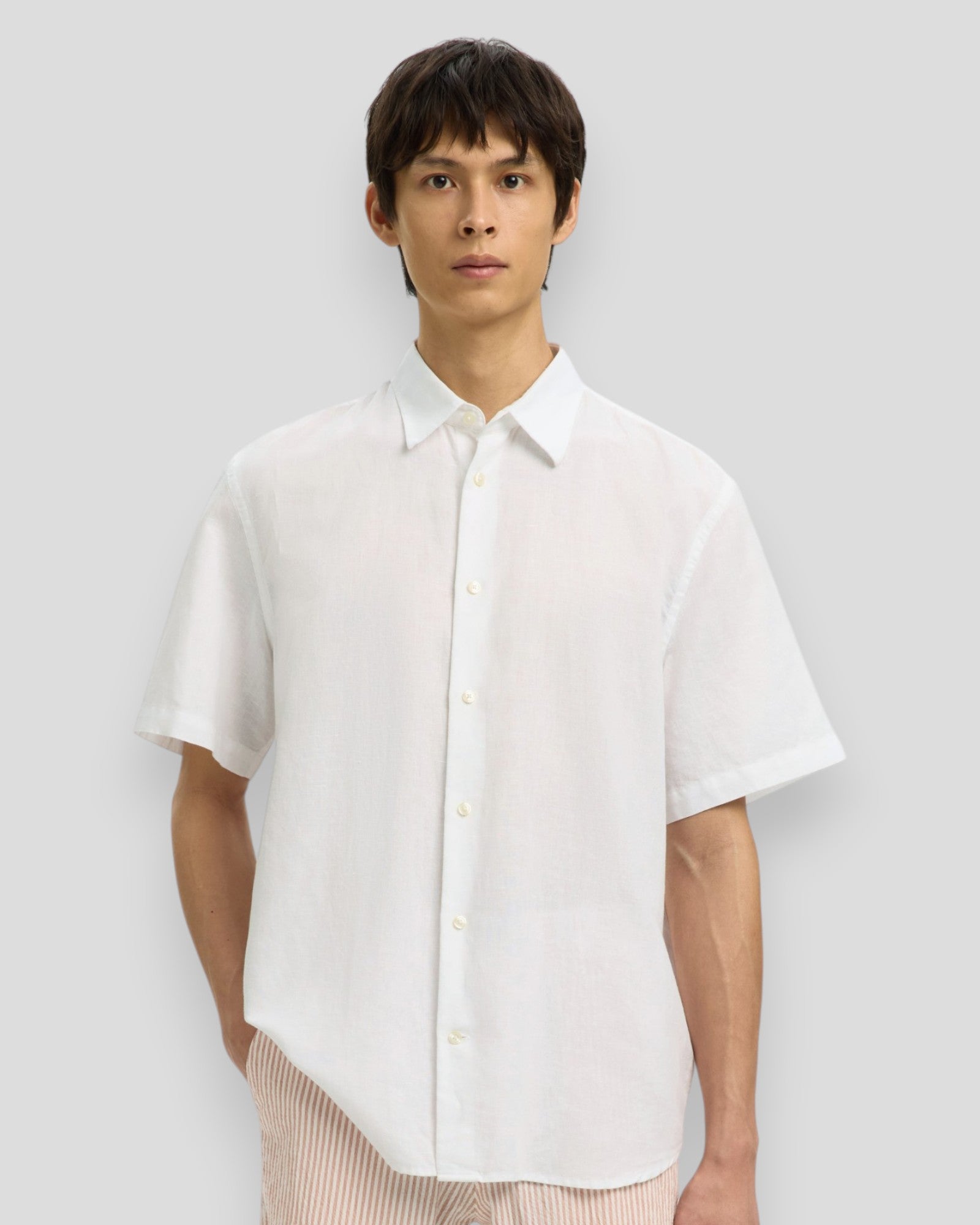 Bright white Selected men's Claus Clay linen blend short-sleeve shirt displayed on a hanger, showcasing its lightweight, casual design.