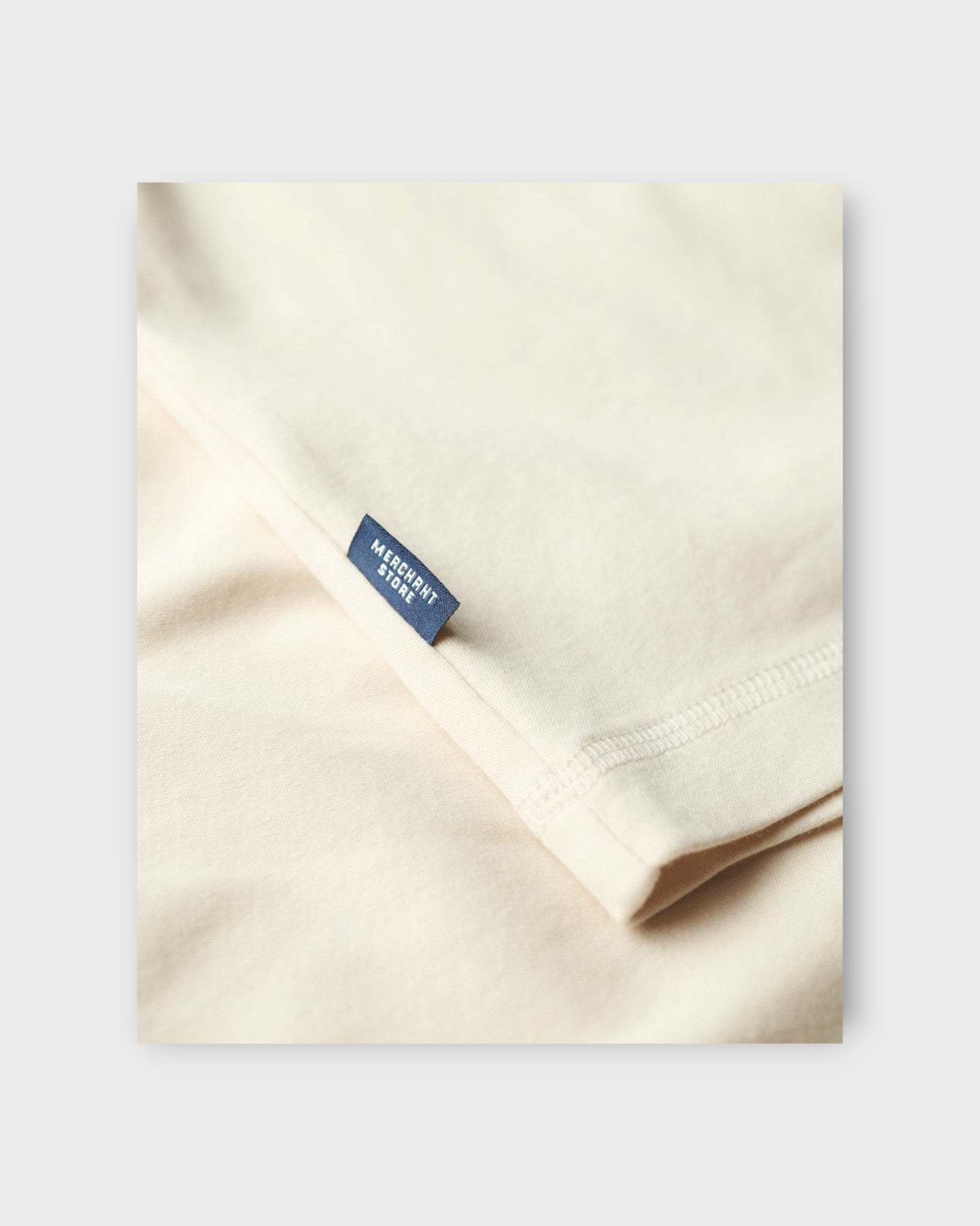 Merchant Jersey Grandad Top Oatmeal Beige fra Superdry. Sandfarvet lang ærmet T-shirt med knaplukning ved halsen. Her ses label på T-shirten.