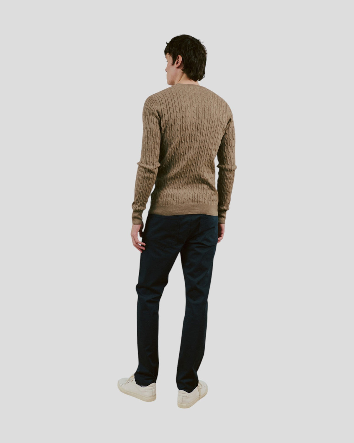 The Sons online Guizchou brown cable knit sweater worn by a man with dark trousers and white sneakers, back view