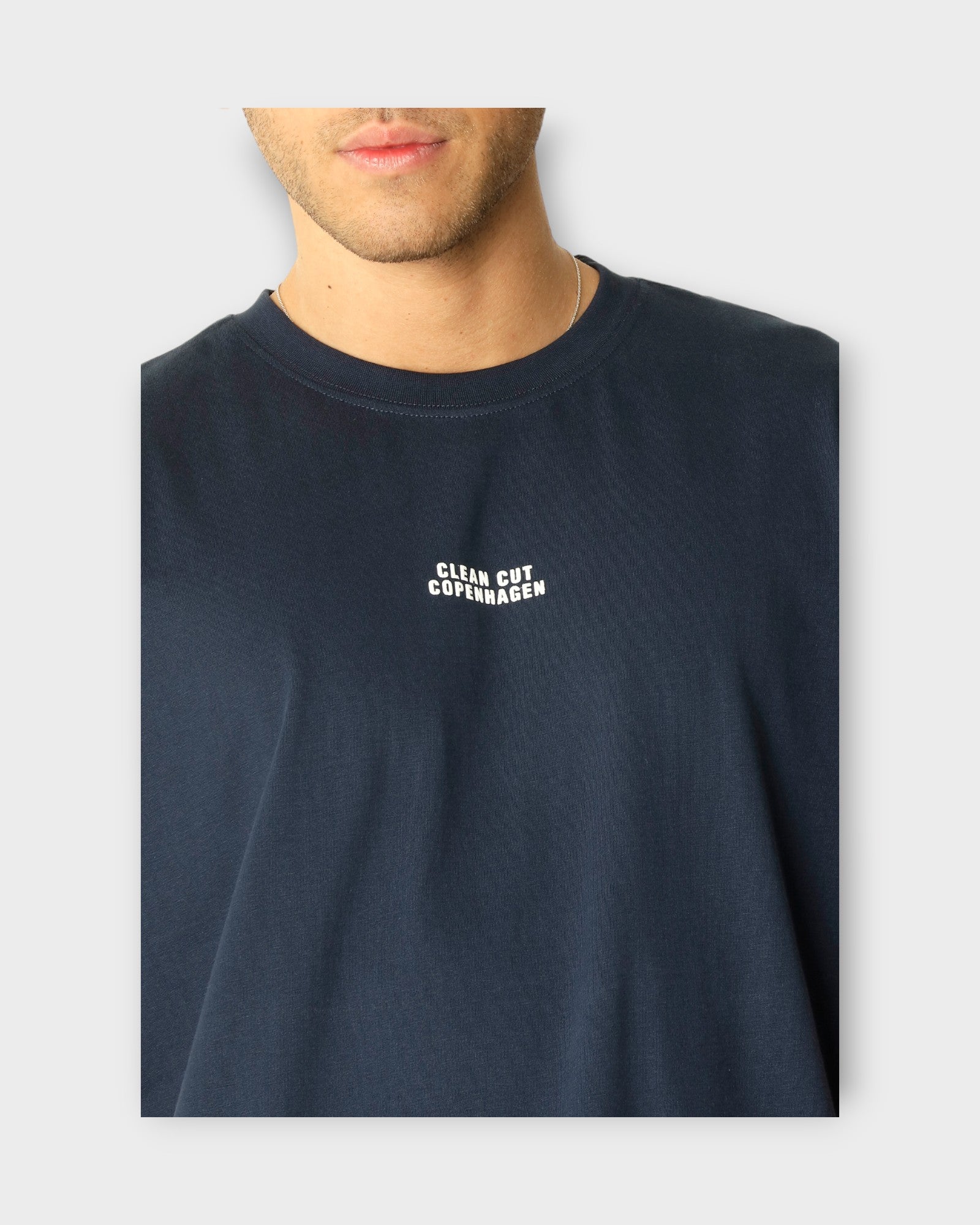 Cohen Organic Tee Navy fra Clean Cut Copenhagen. Mørkeblå T-shirt til mænd i regular fit. Her ses logoet i closeup.