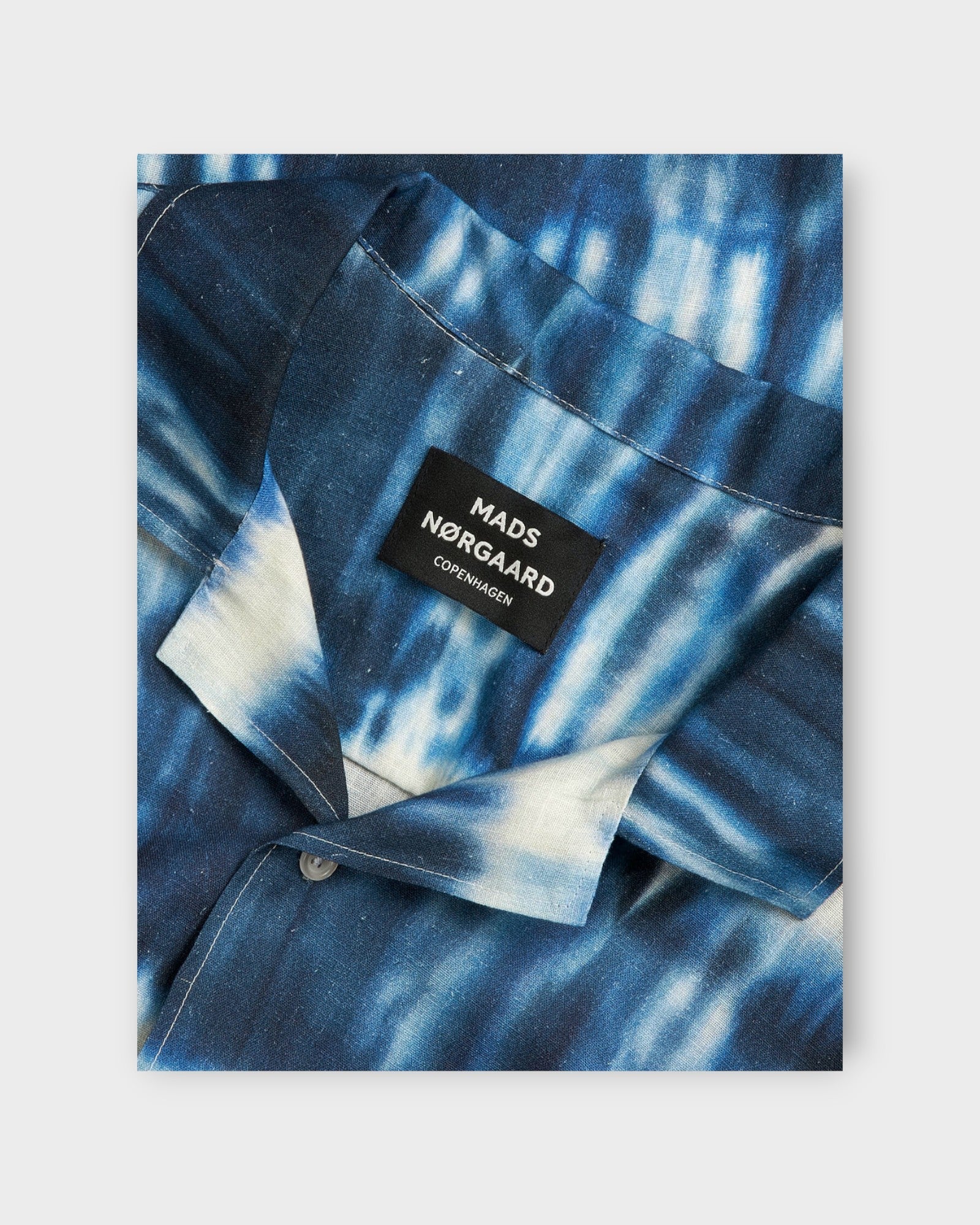 Cotton Linen Kenji Shirt SS Tie Dye Stripe AOP Merthy fra Mads Nørgaard. Kortærmet stribet hørskjorte til mænd. Farverne i striberne er hvid, lyseblå og mørkeblå. Her ses et closeup af label og kvalitet.