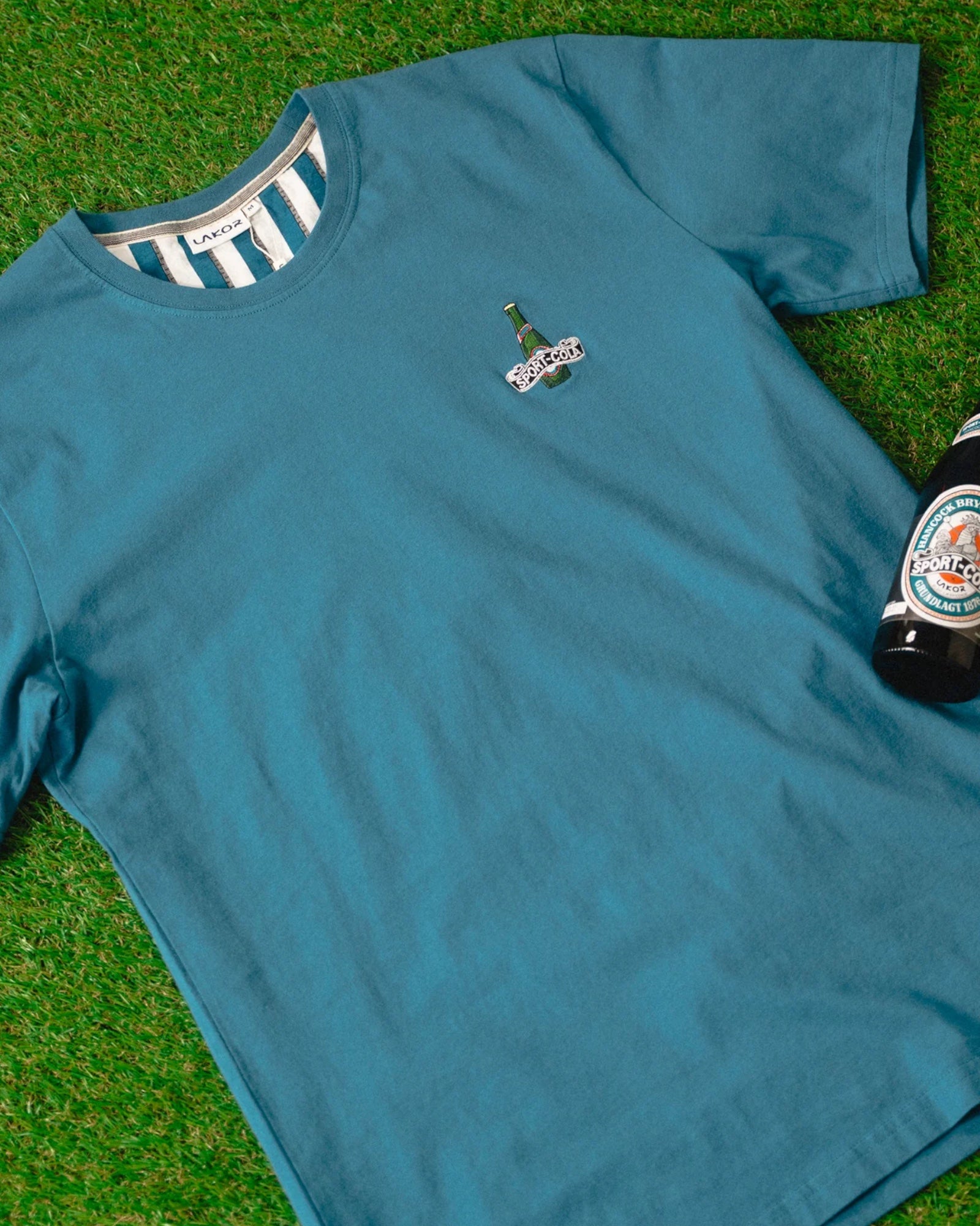 Lakor Mini Bottle Tee i havblå, afslappet t-shirt med minimalistisk design, synligt i billedet.