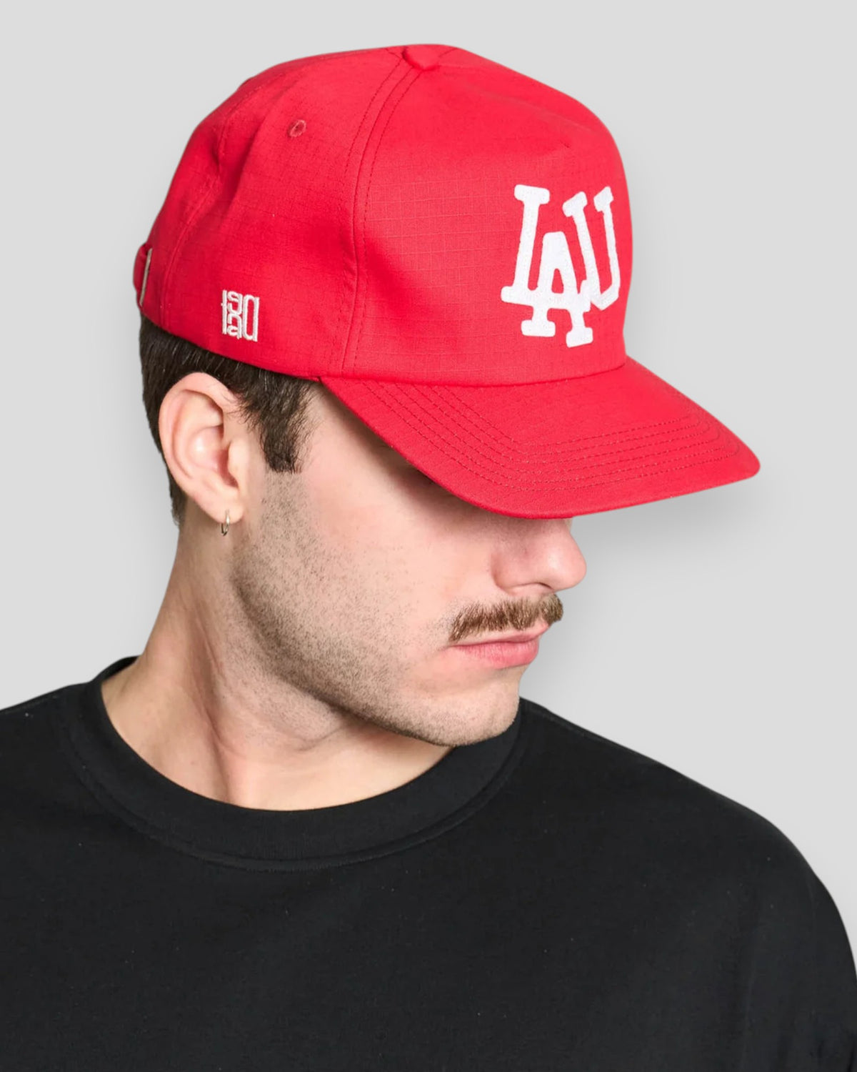 Rød baseball cap fra Lau Lau med needlepunch-materiale, vist i et close-up billede.